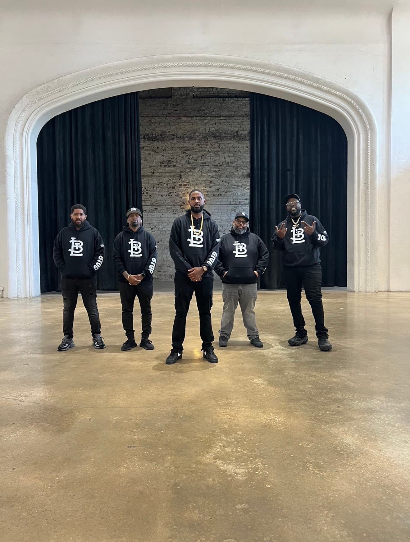 Five artists in Broadway hoodies posing together on a stage
